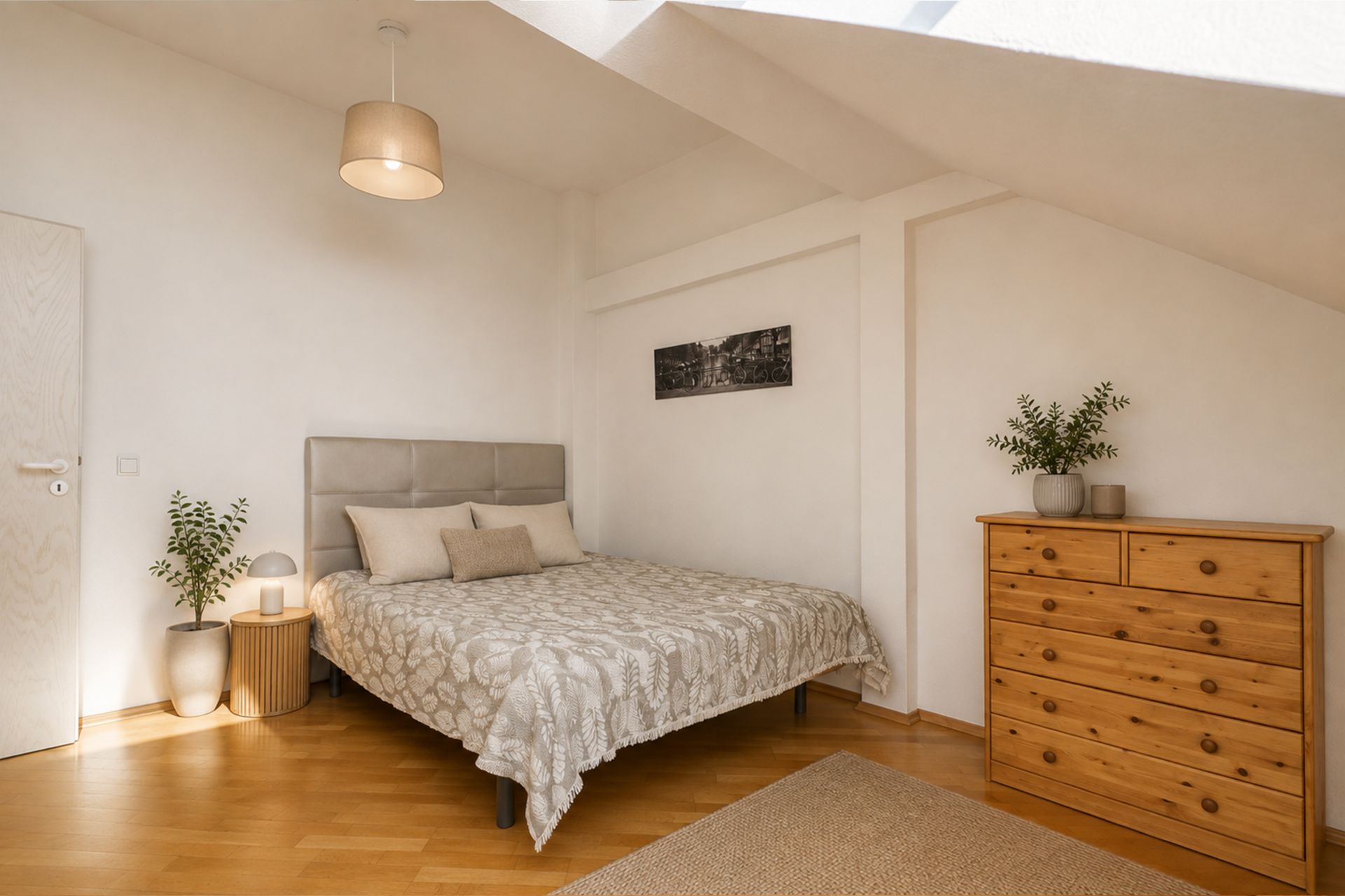Helles Schlafzimmer mit Doppelbett, Holzkommode, Pflanzen und schräger Decke.