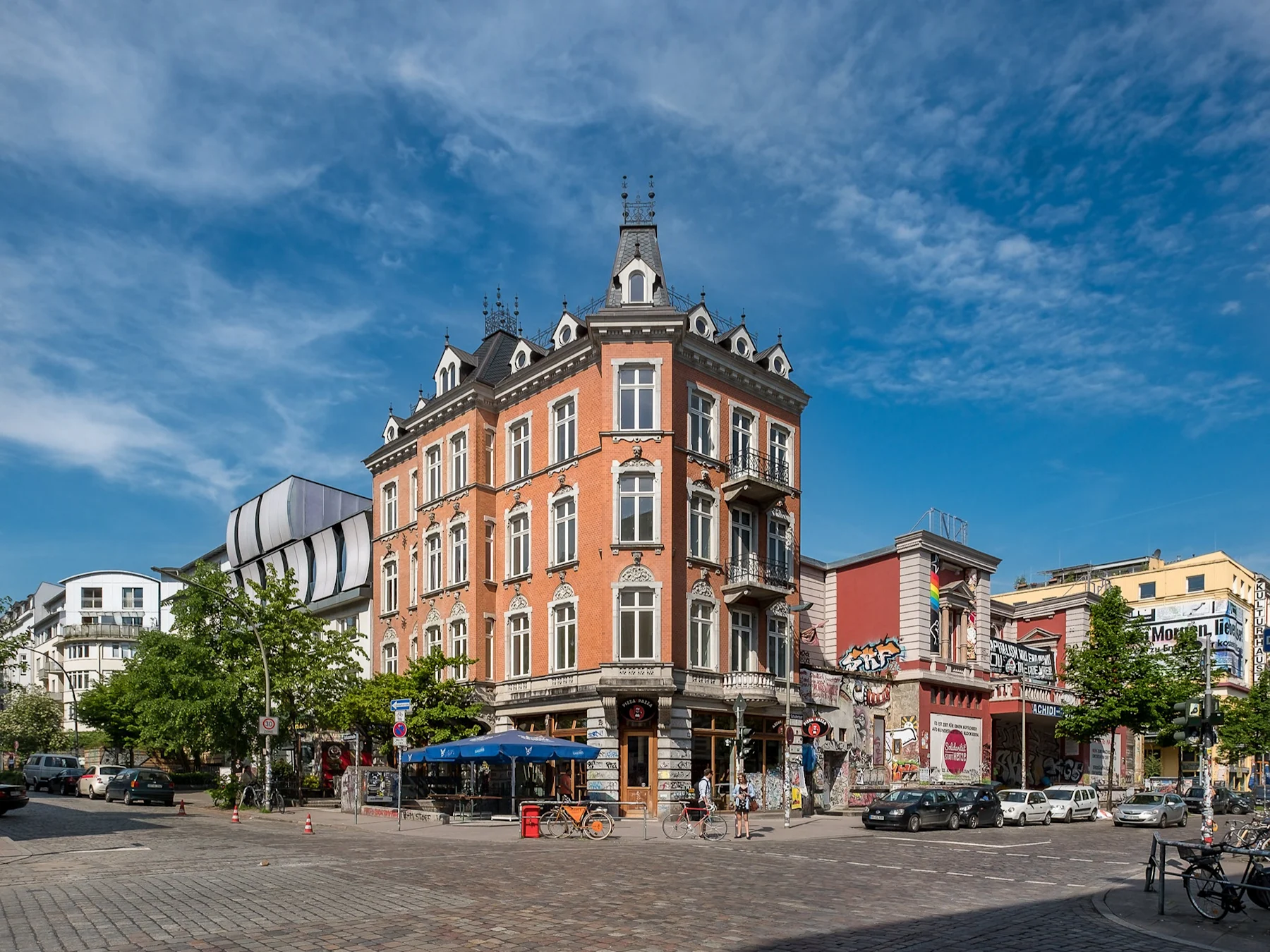Eckhaus mit Balkon, verzierten Fenstern und Geschäften im Erdgeschoss an einer Straßenecke.