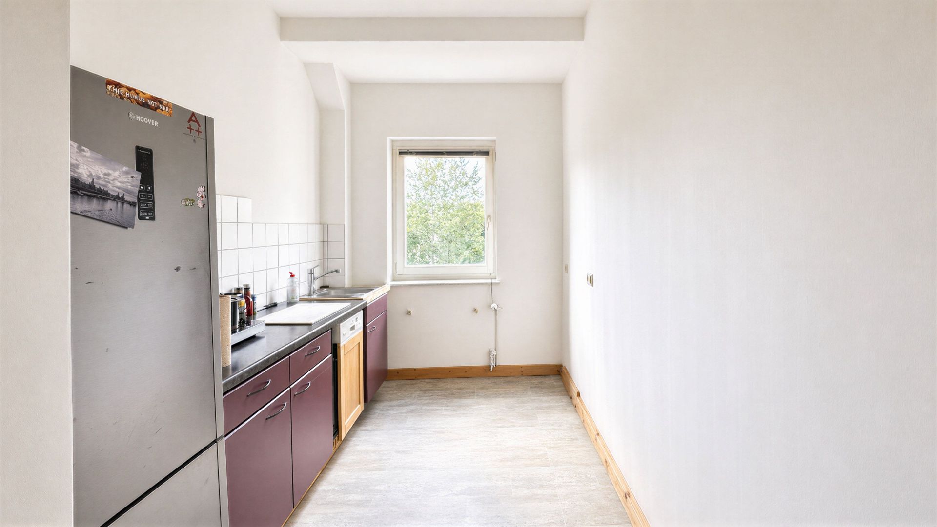 Schmale Küche mit lila Unterschränken, grauem Kühlschrank und Fenster am Ende.