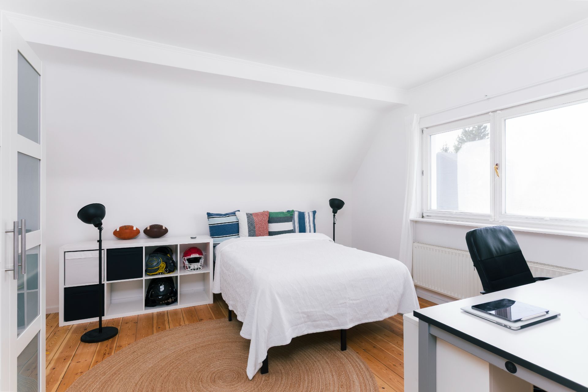 Helles Schlafzimmer mit Bett, Schreibtisch, Fenster und Regal auf Holzboden.