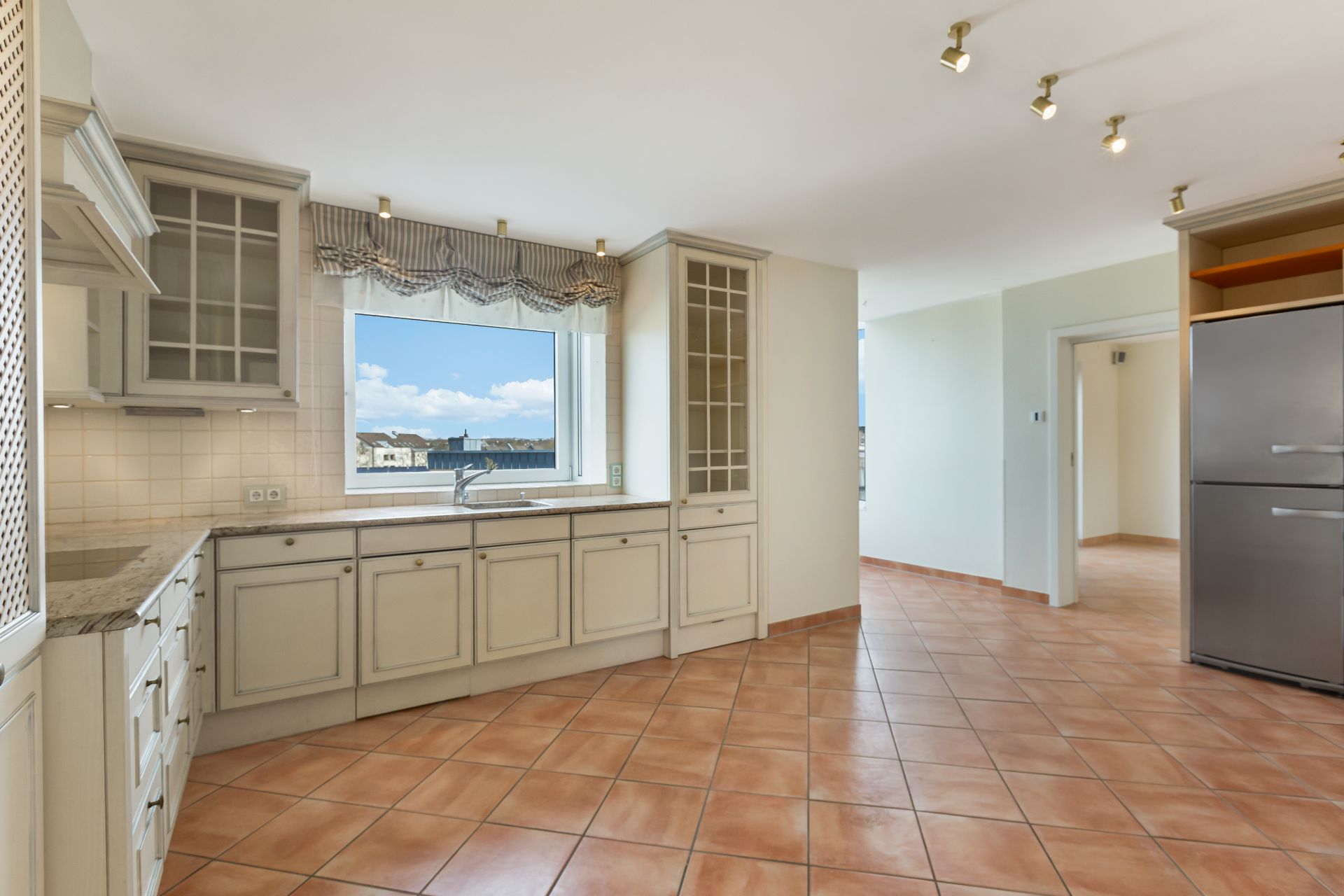 Helle Küche mit Fliesenboden, Einbauschränken, Fenster und Edelstahlkühlschrank.