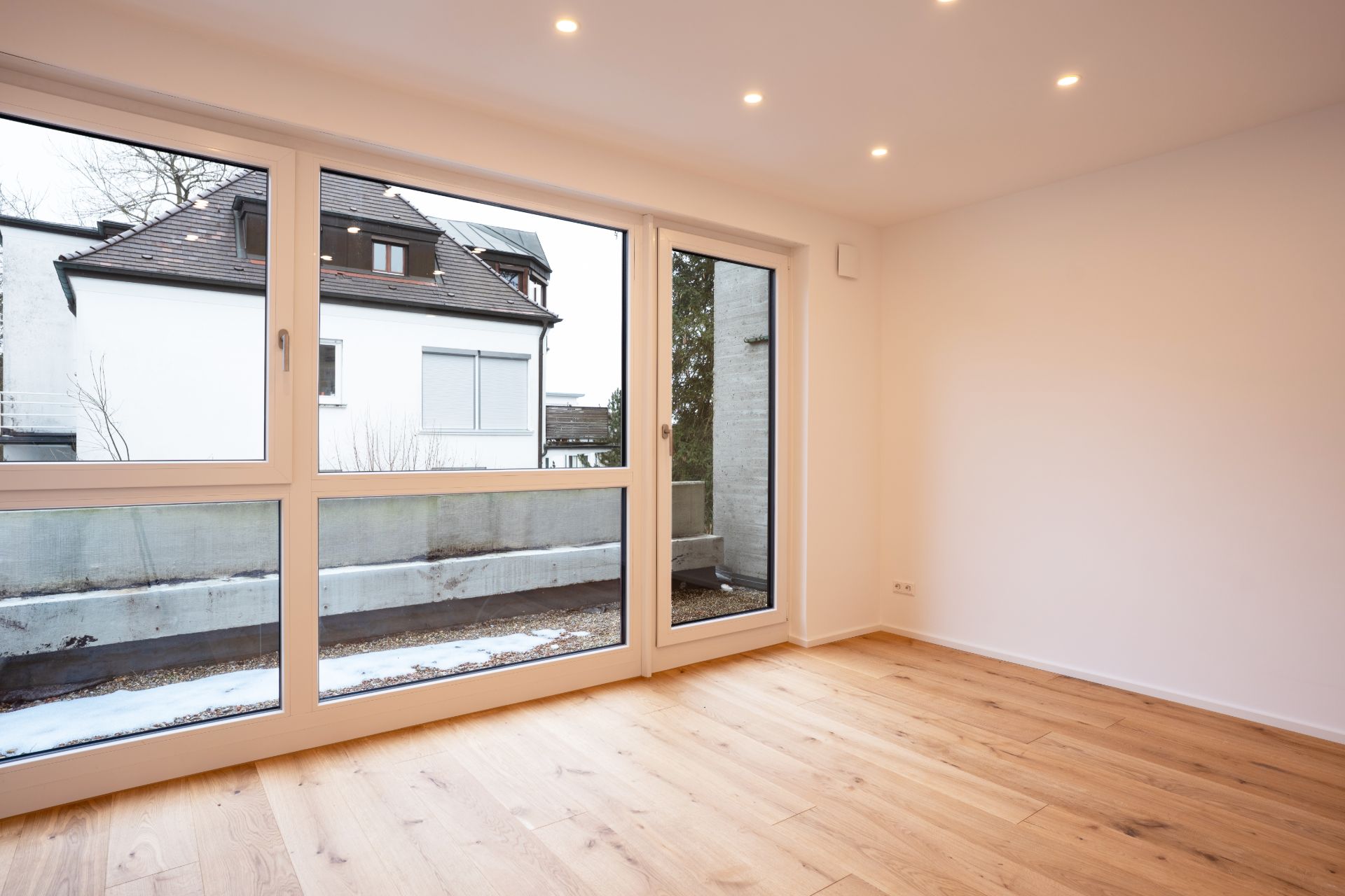 Leerer, heller Raum mit Holzfußboden und großen Fenstern, die auf einen Balkon führen.