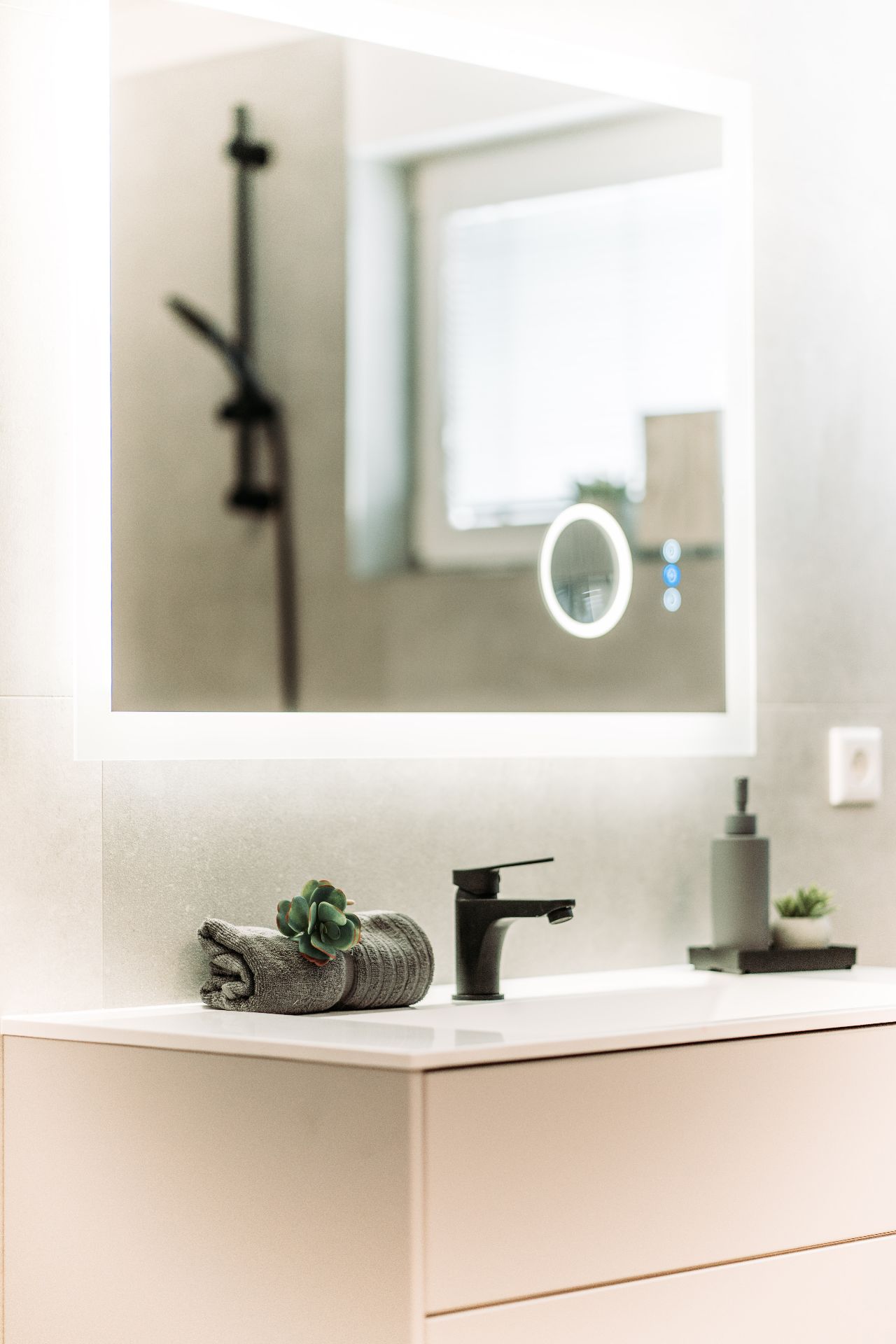 Modernes Badezimmer mit beleuchtetem Spiegel, Waschbecken, schwarzem Wasserhahn und Handtuch mit Pflanze.