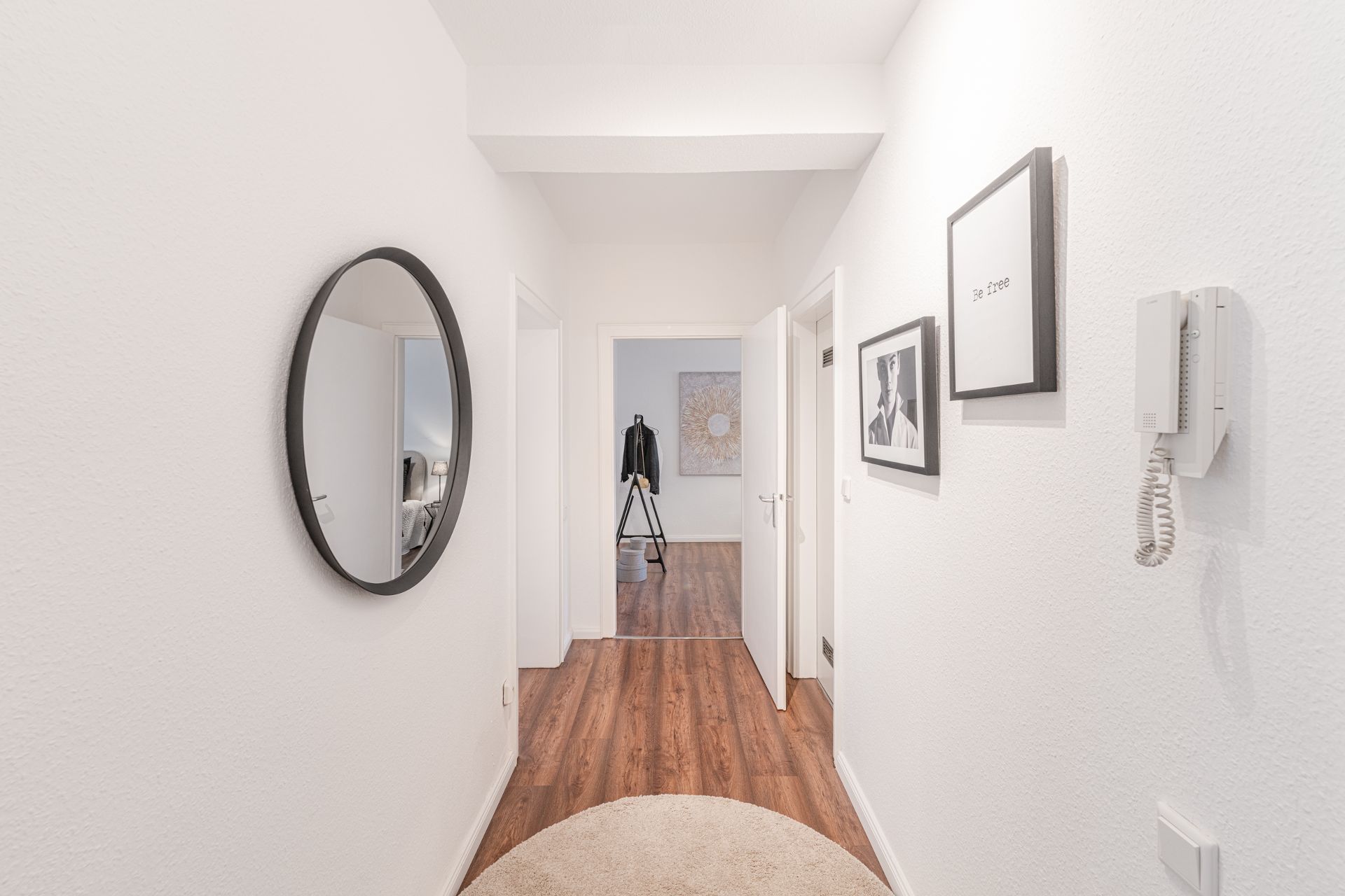 Heller Flur mit rundem Spiegel, Holzboden und Bildern an der Wand.