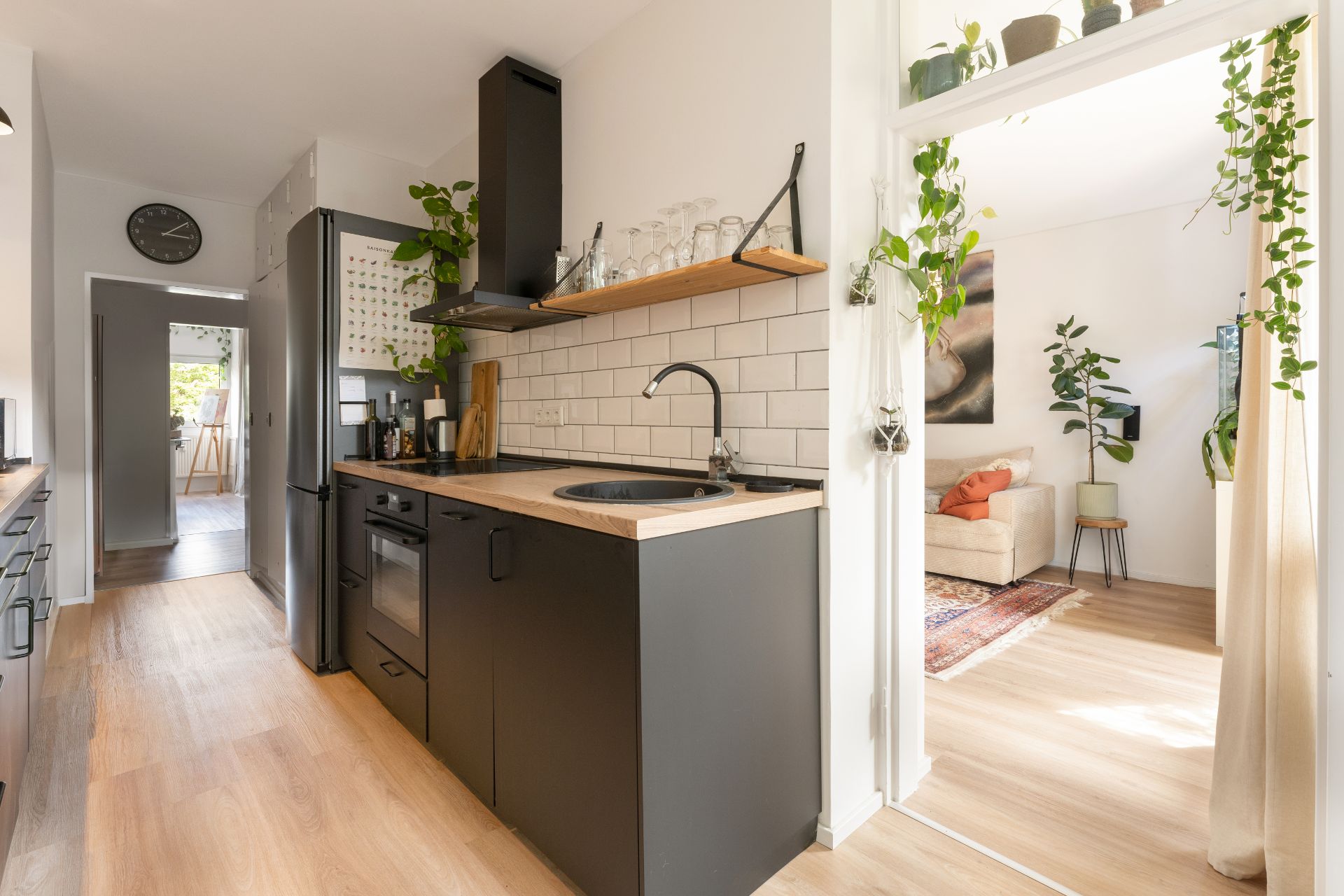 Moderne Küche mit schwarzen Schränken, Holzboden, Pflanzen und Blick ins helle Wohnzimmer.