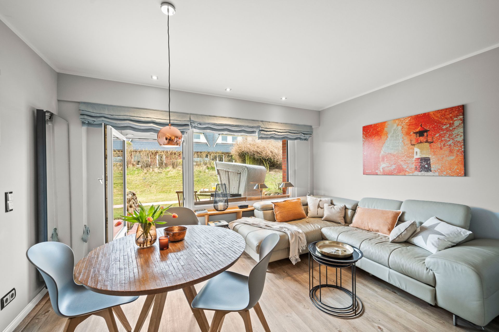 Helles Wohnzimmer mit Sofa, rundem Esstisch und großen Fenstern zum Garten.