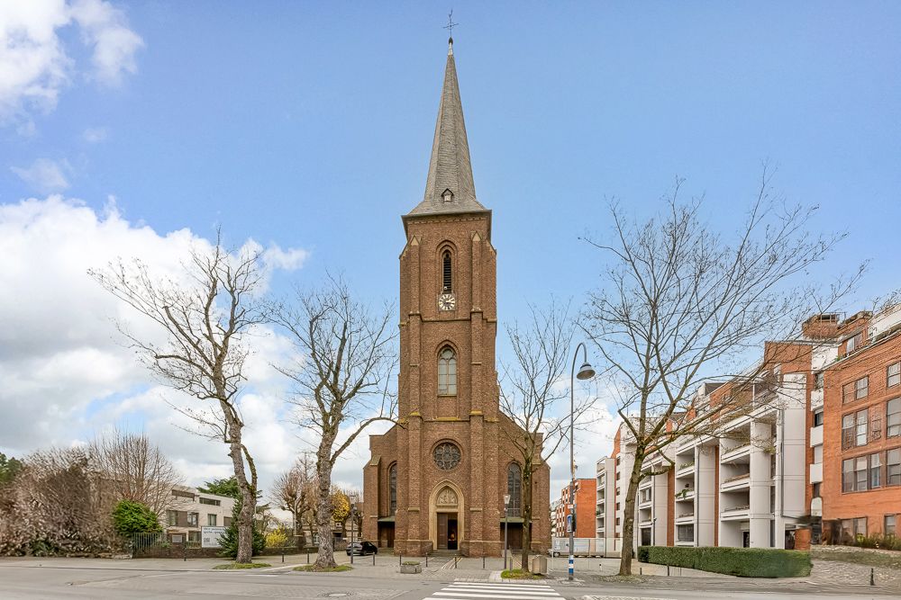 Backsteinkirche mit hohem Turm und Uhr, umgeben von kahlen Bäumen und Wohngebäuden.