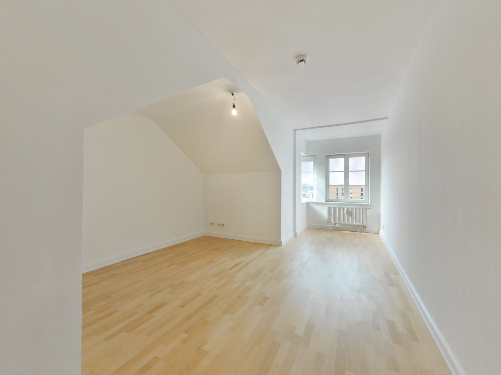 Heller, leerer Raum mit weiß gestrichenen Wänden, Holzfußboden und Fenster am Ende.