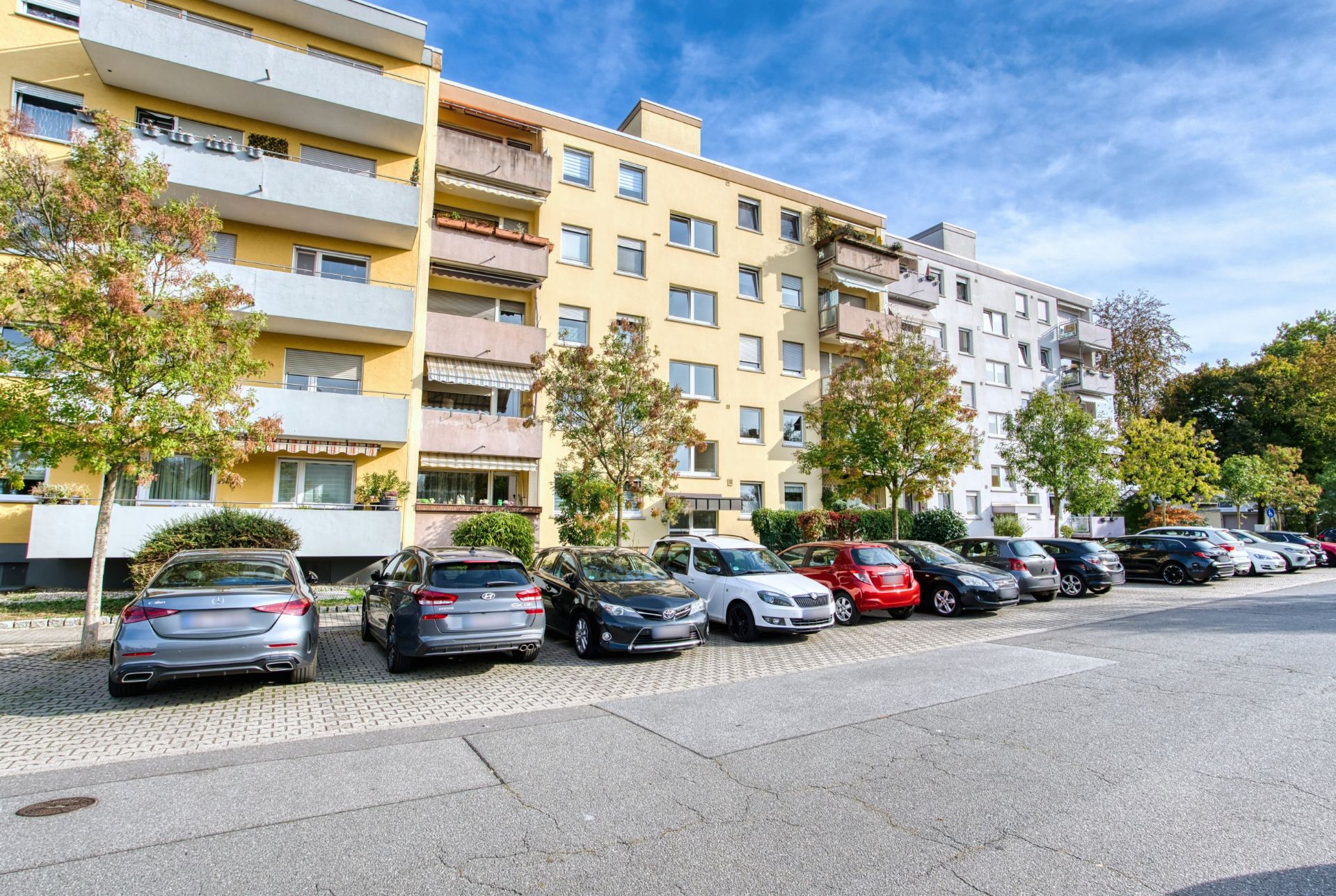 Mehrstöckiges Wohnhaus mit Balkonen und parkenden Autos davor.