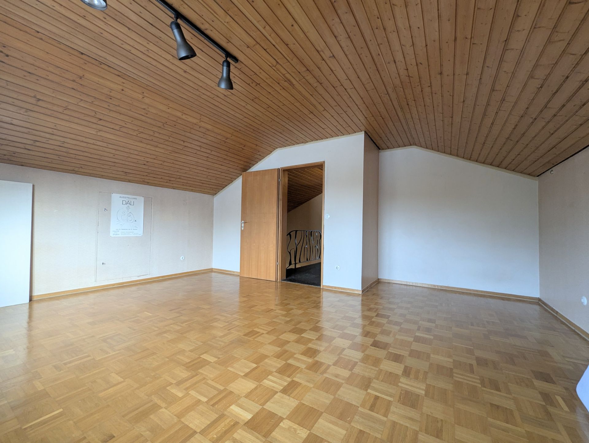 Leeres Zimmer mit Holzdecke, Parkettboden und offenem Türrahmen.