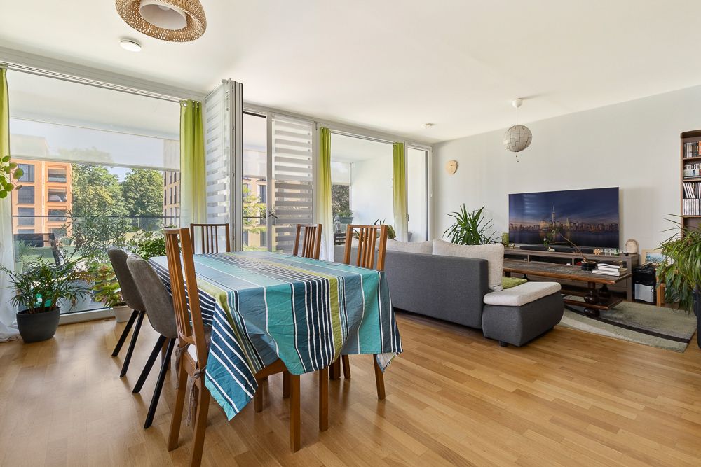 Helles Wohnzimmer mit Esstisch, Stühlen, Sofa, Fernseher und vielen Pflanzen.