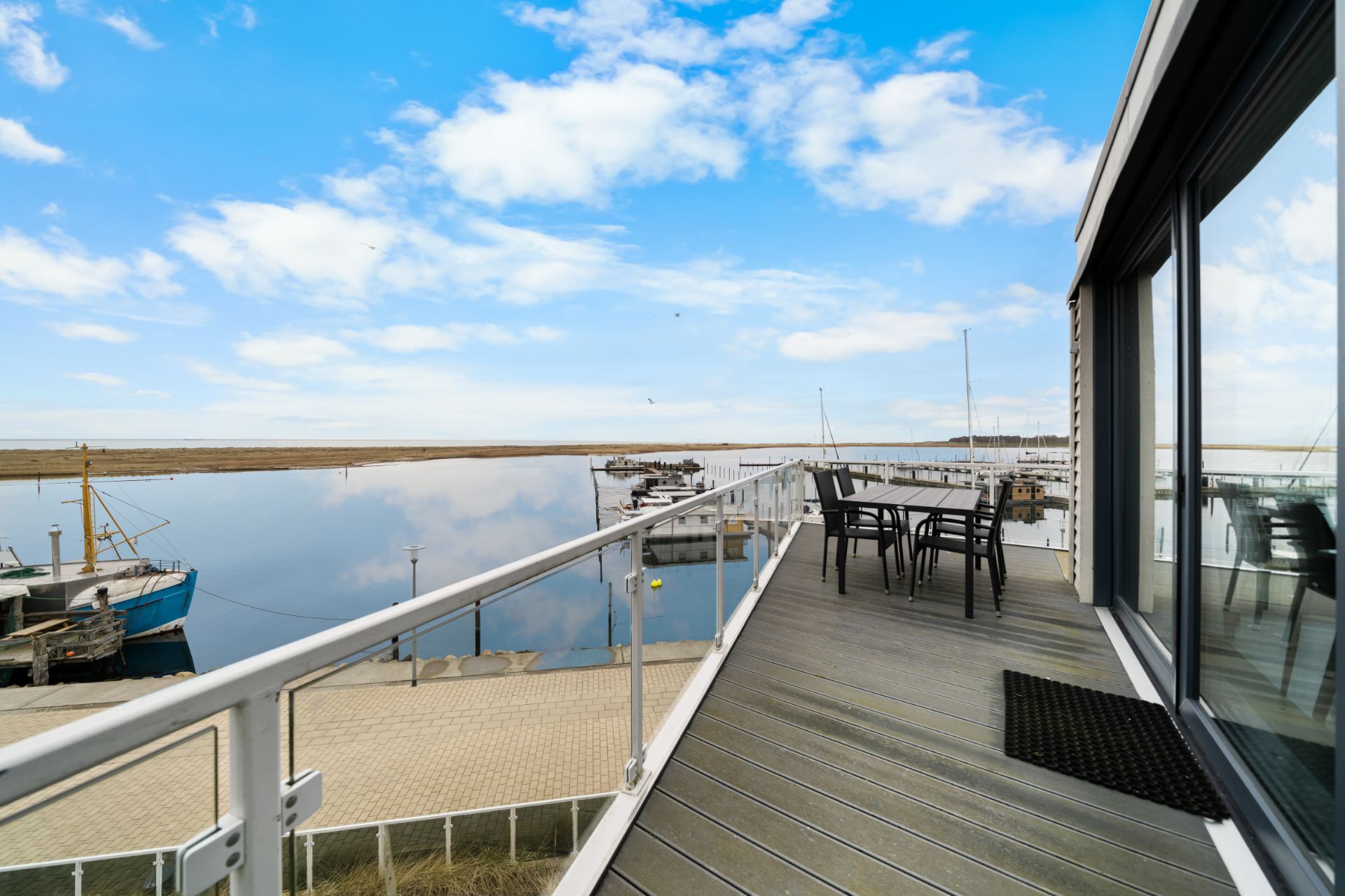 Großer Balkon mit Tisch und Stühlen, Blick auf einen ruhigen Hafen und das Wasser.