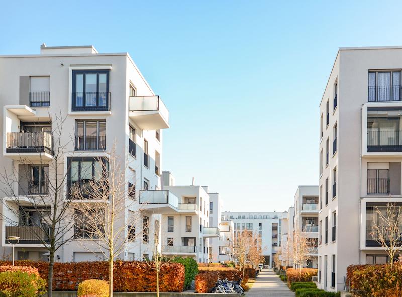 Moderne Wohngebäude mit Balkonen und einem gepflasterten Weg zwischen Gartenanlagen.