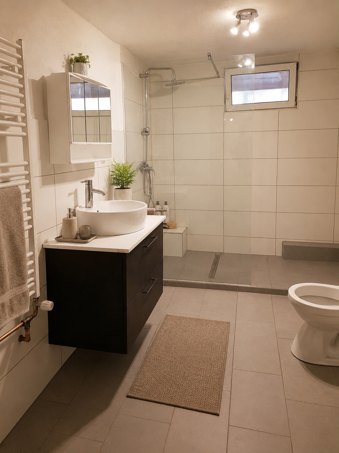 Modernes Badezimmer mit Dusche, Waschbecken, WC und Spiegel, Fliesenboden und kleinem Fenster.