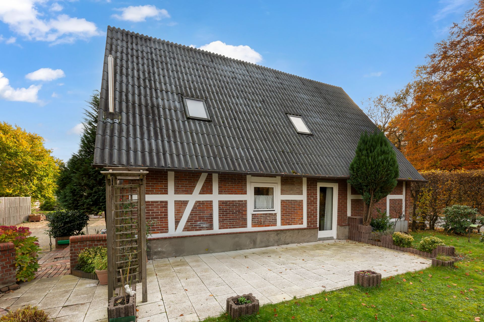 Ein Einfamilienhaus mit Satteldach, roter Backsteinfassade und Terrasse im Garten.