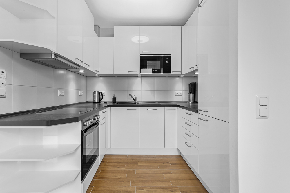 Moderne weiße Einbauküche mit Herd, Mikrowelle und Holzfußboden.
