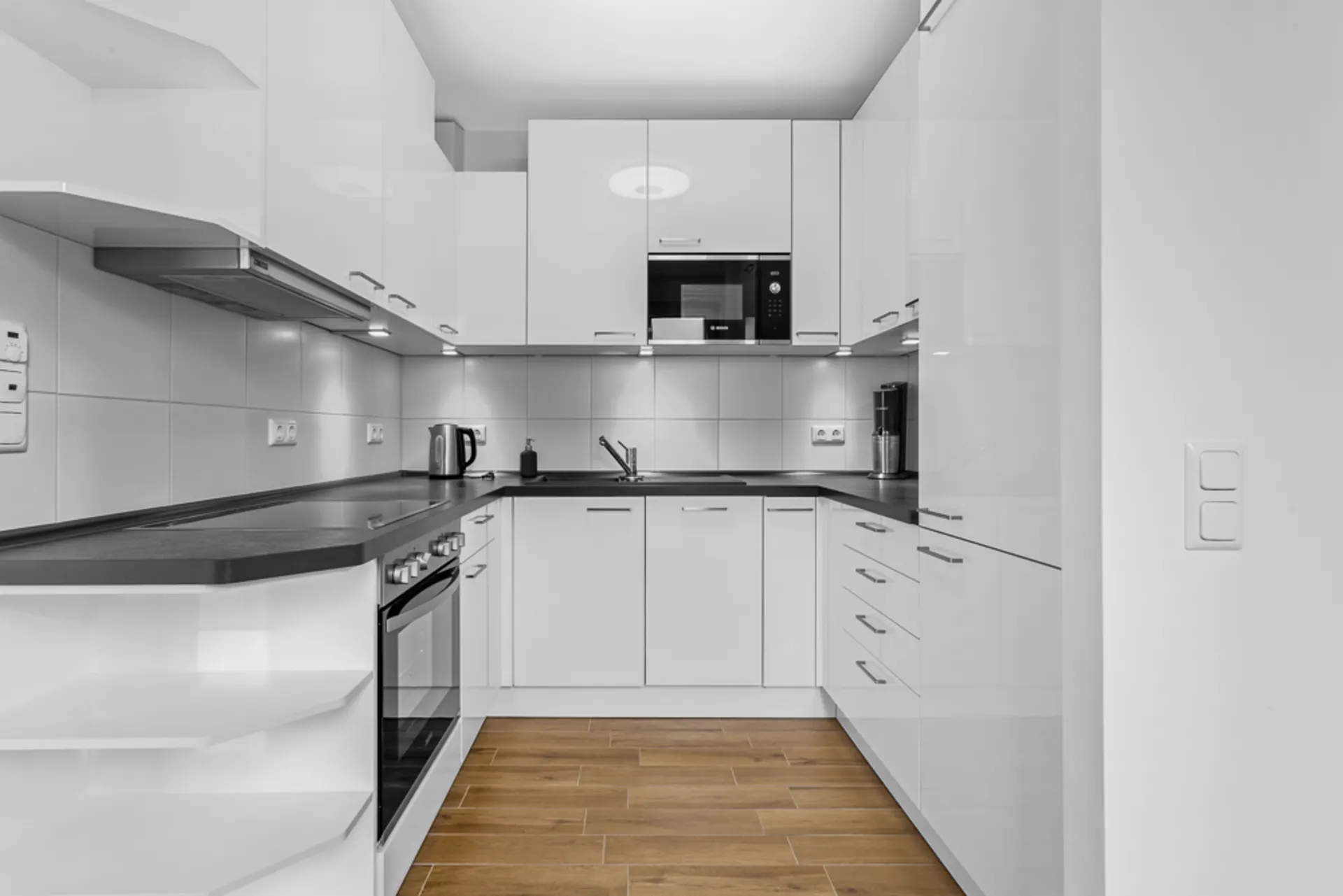 Moderne weiße Einbauküche mit Herd, Mikrowelle und Holzfußboden.