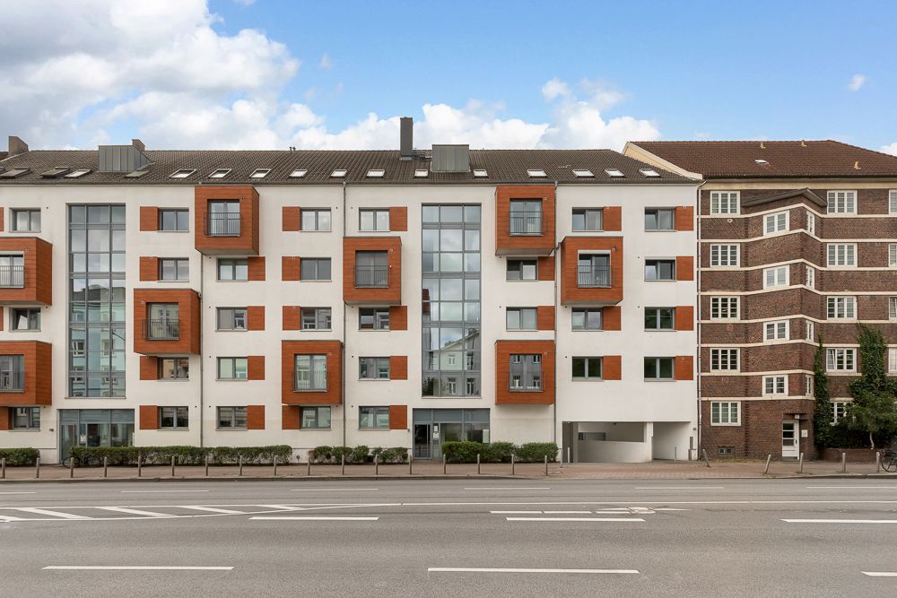 Modernes Wohngebäude mit weißen Fassaden und orangen Fensterrahmen an einer Straße.