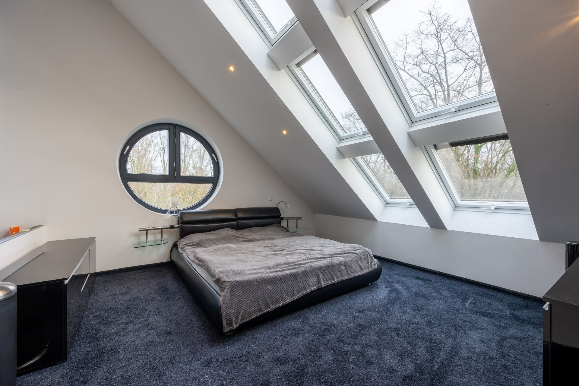 Modernes Schlafzimmer mit schrägem Dach, großen Dachfenstern und rundem Fenster.