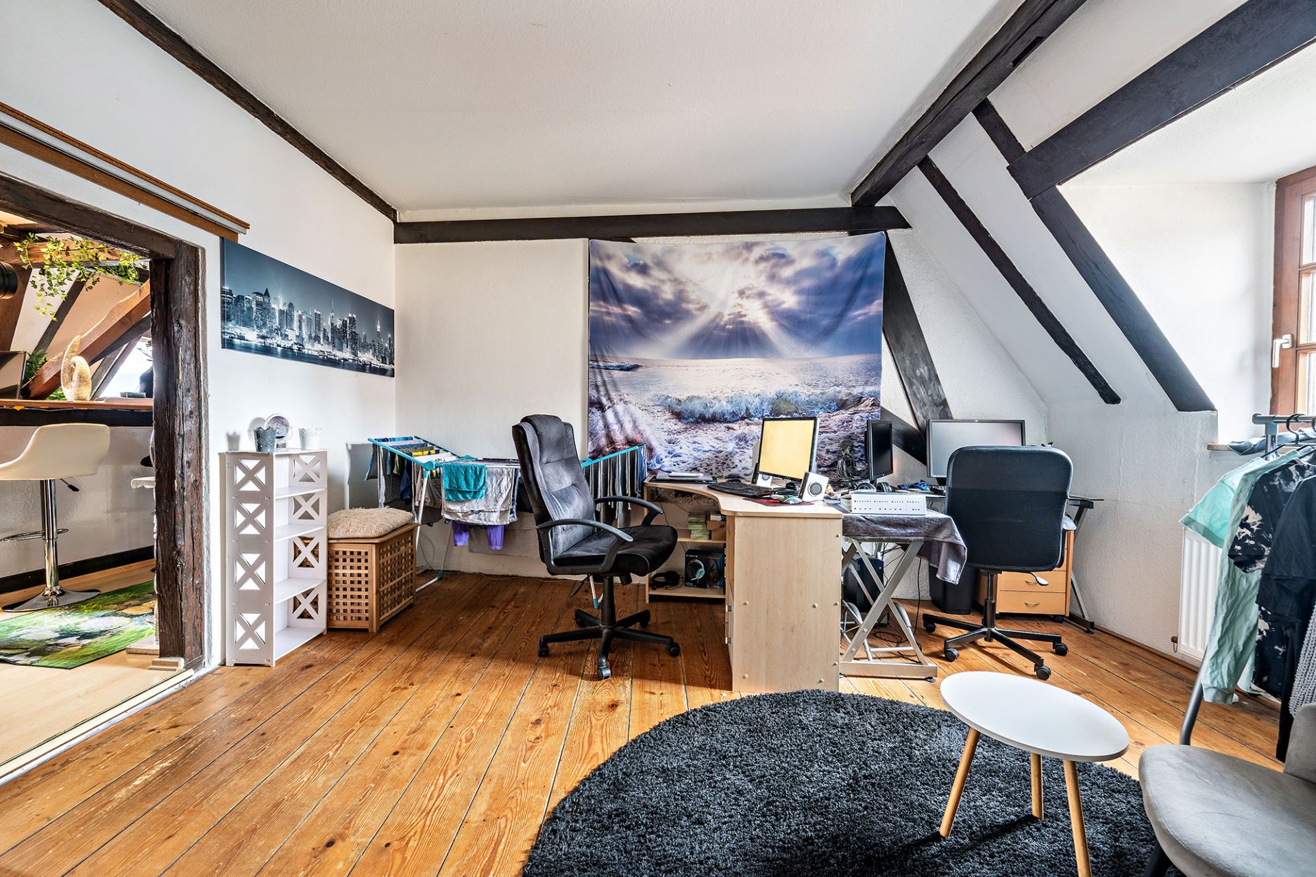 Helles Arbeitszimmer mit zwei Schreibtischen, Bürostühlen, Holzfußboden und Wandbild mit Meer.