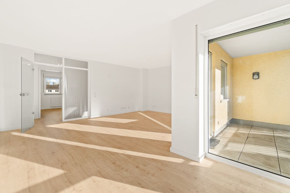 Helles Wohnzimmer mit Holzfußboden, Zugang zum Balkon, offene Tür zu weiterem Zimmer.