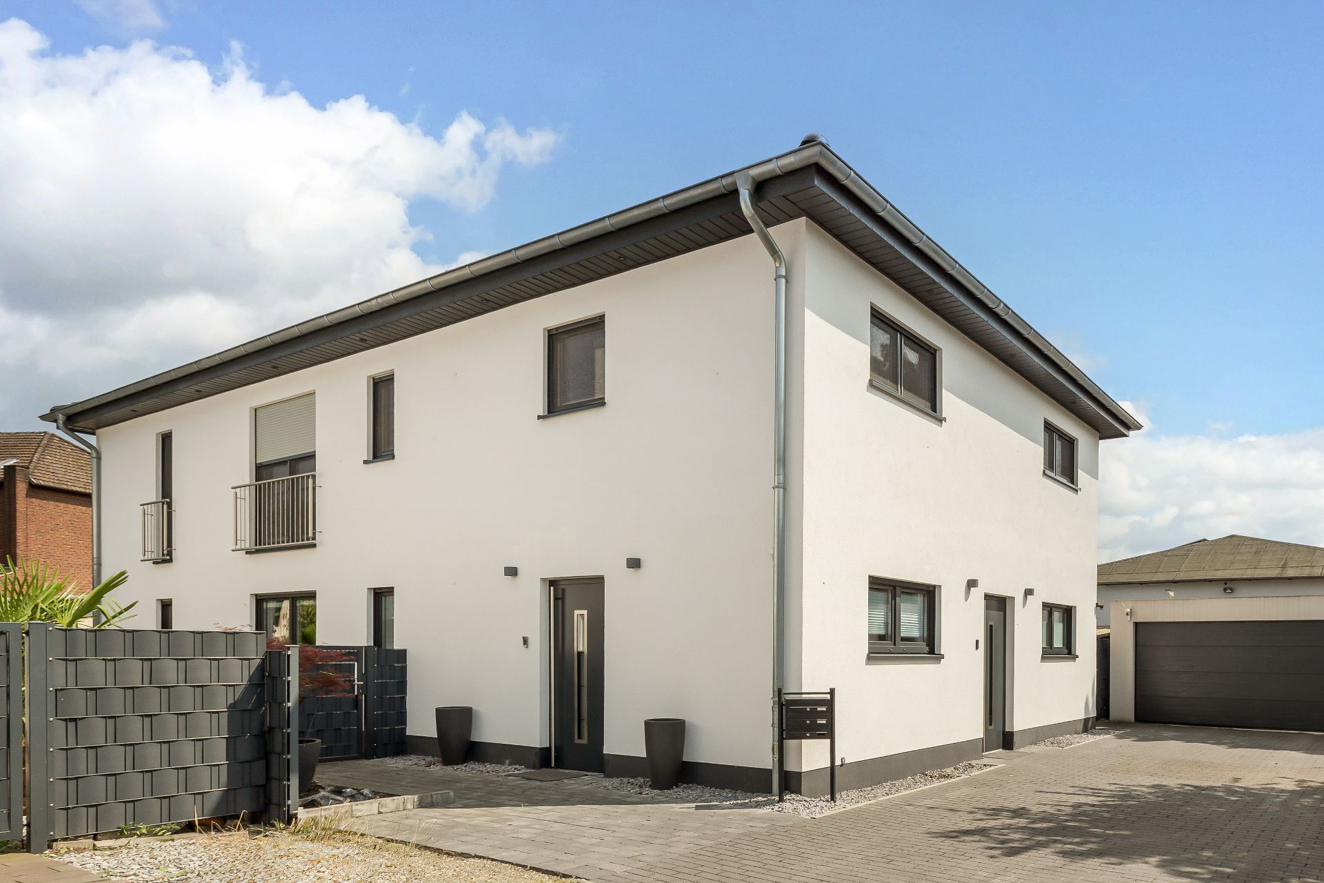 Modernes, zweistöckiges Wohnhaus mit weißer Fassade und schwarzem Dach, gepflasterter Einfahrt.
