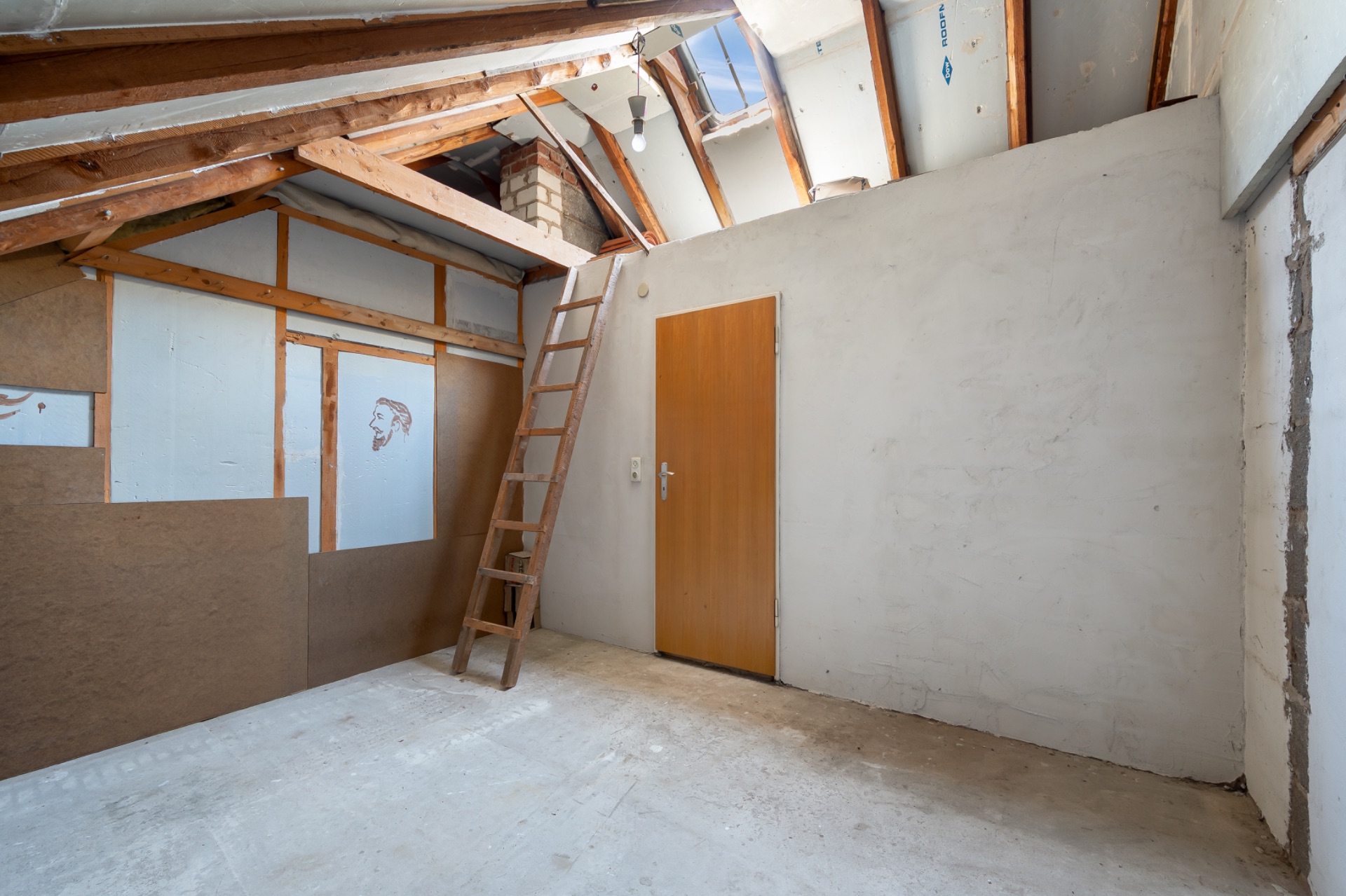 Ein Dachbodenraum mit Holzleiter, Holzbalken, Tür und sichtbarem Fenster im Dach.