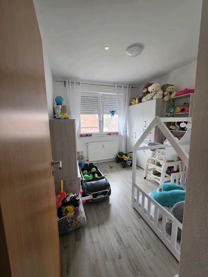 Kinderzimmer mit Spielzeug, Bett in Hausform, Kuscheltieren und großen Fenstern.