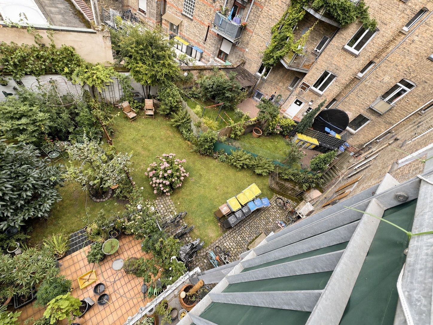 Blick in einen begrünten Innenhof mit Rasen, Mülltonnen und Sitzgelegenheiten.