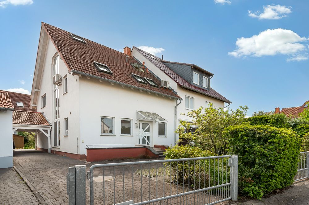 Zweistöckiges Wohnhaus mit rotem Dach, Vorgarten und Einfahrt hinter einem Metallzaun.