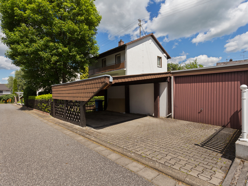 Offener Carport und Garage vor einem Wohnhaus mit gepflasterter Einfahrt.