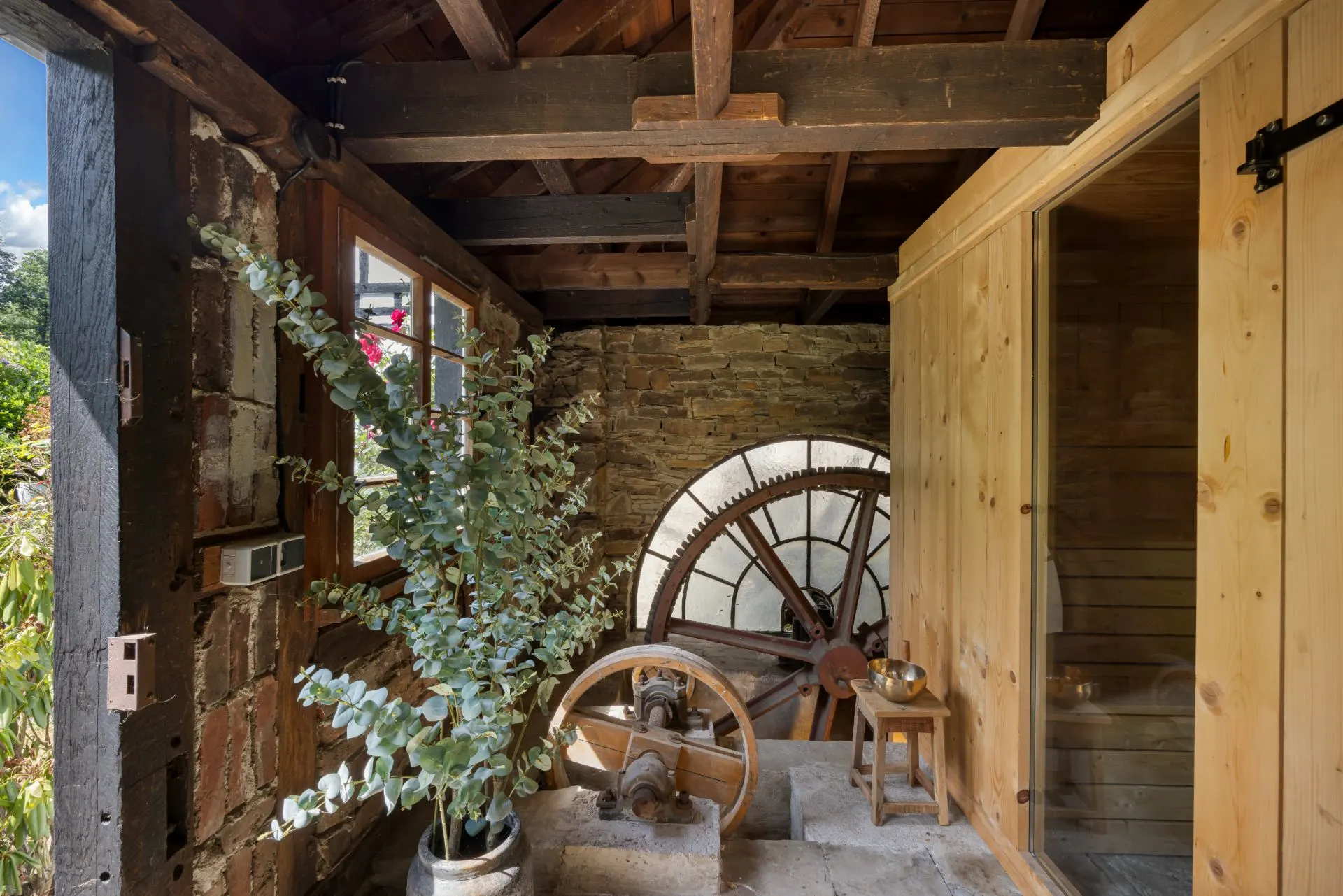 Innenraum mit großem Zahnrad, Holzwänden, Steinwand und Topfpflanze.