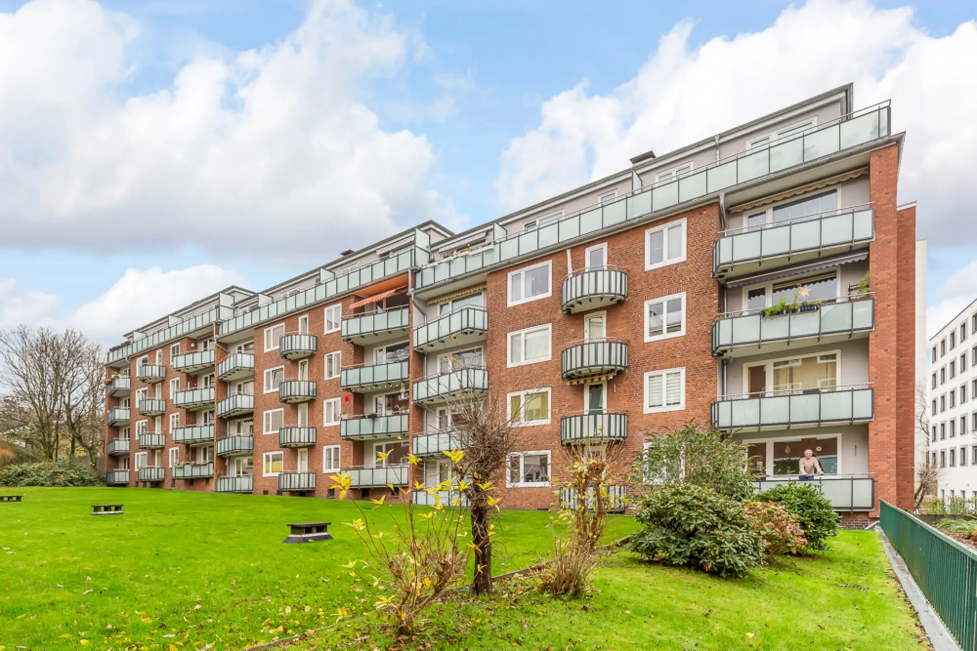 Mehrstöckiges Wohnhaus mit Balkonen und gepflegtem grünen Garten im Vordergrund.