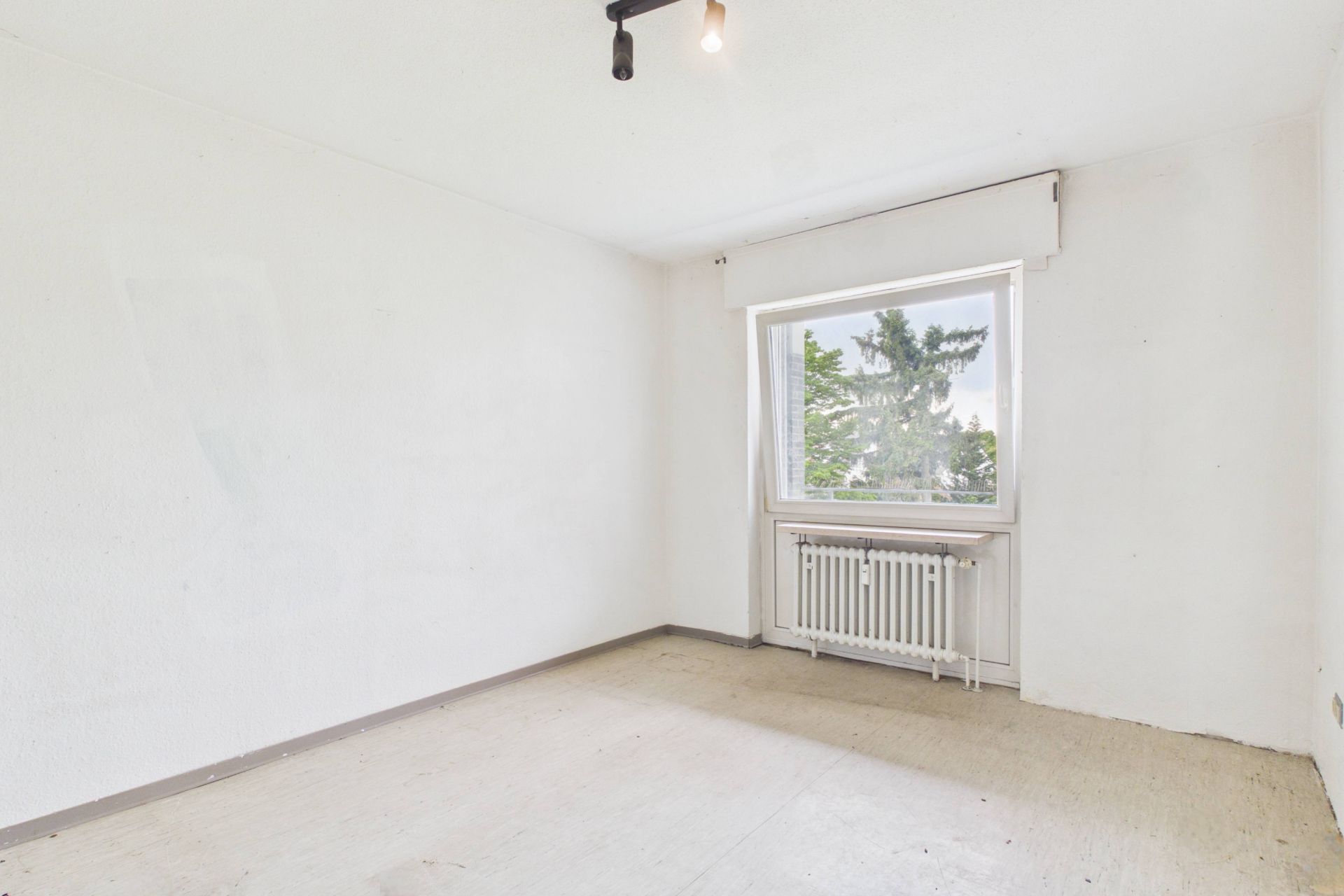 Leeres, helles Zimmer mit großem Fenster und Heizung unter dem Fenster.