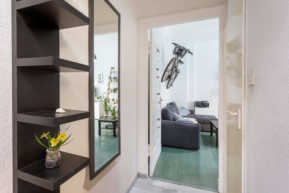 Flur mit Regal und Spiegel, Blick ins Wohnzimmer mit Sofa und aufgehängtem Fahrrad.