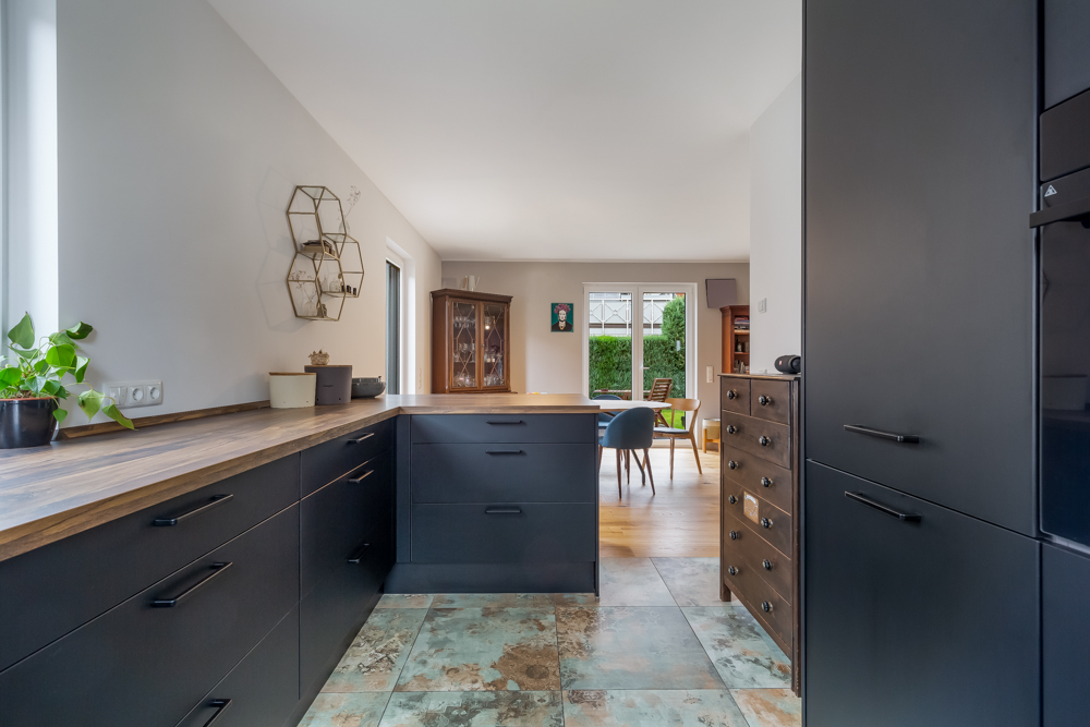 Moderne Küche mit dunklen Schränken, Holzarbeitsplatte und offener Blick ins Esszimmer.