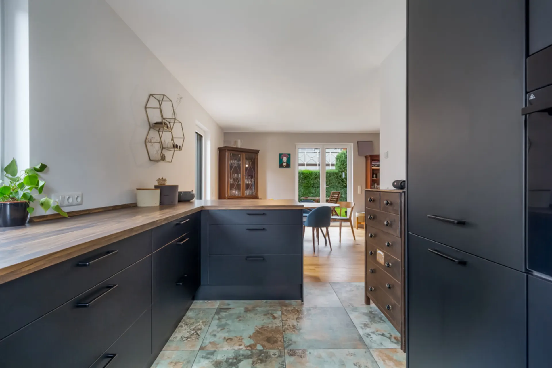 Moderne Küche mit dunklen Schränken, Holzarbeitsplatte und offener Blick ins Esszimmer.