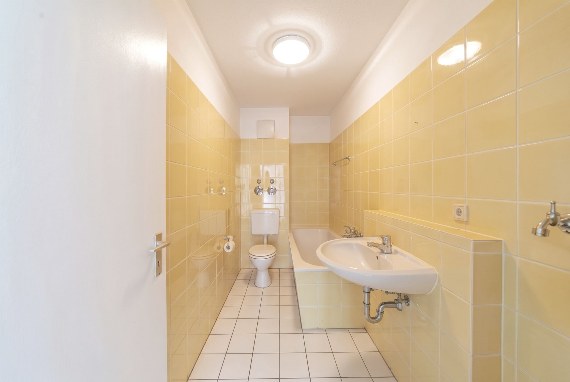 Helles Badezimmer mit gelben Fliesen, Badewanne, Waschbecken und Toilette.