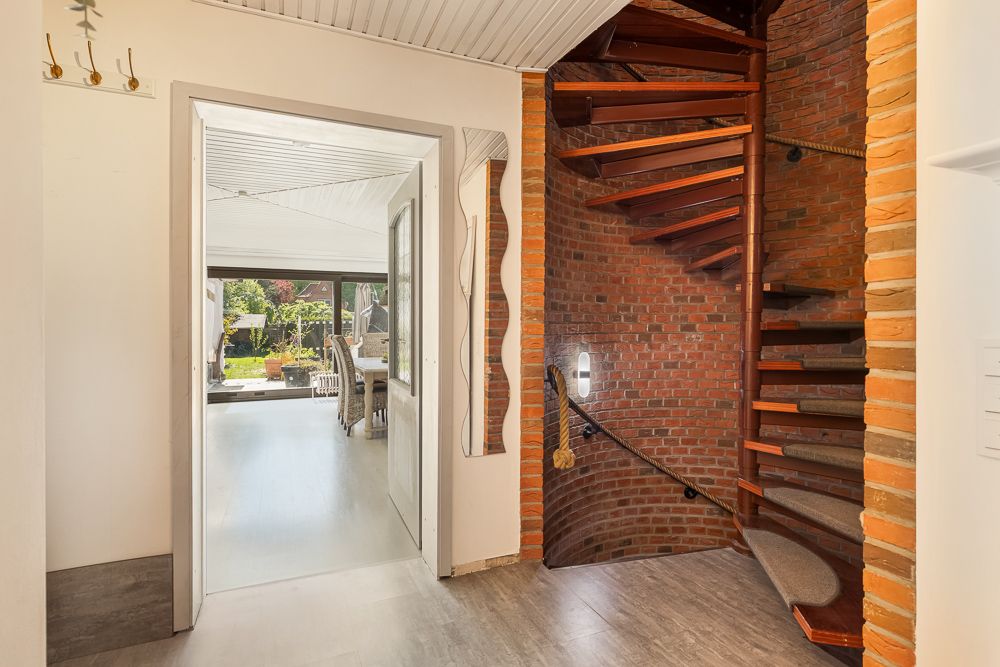 Flur mit gewendelter Holztreppe und Blick in ein helles Wohnzimmer mit Garten.