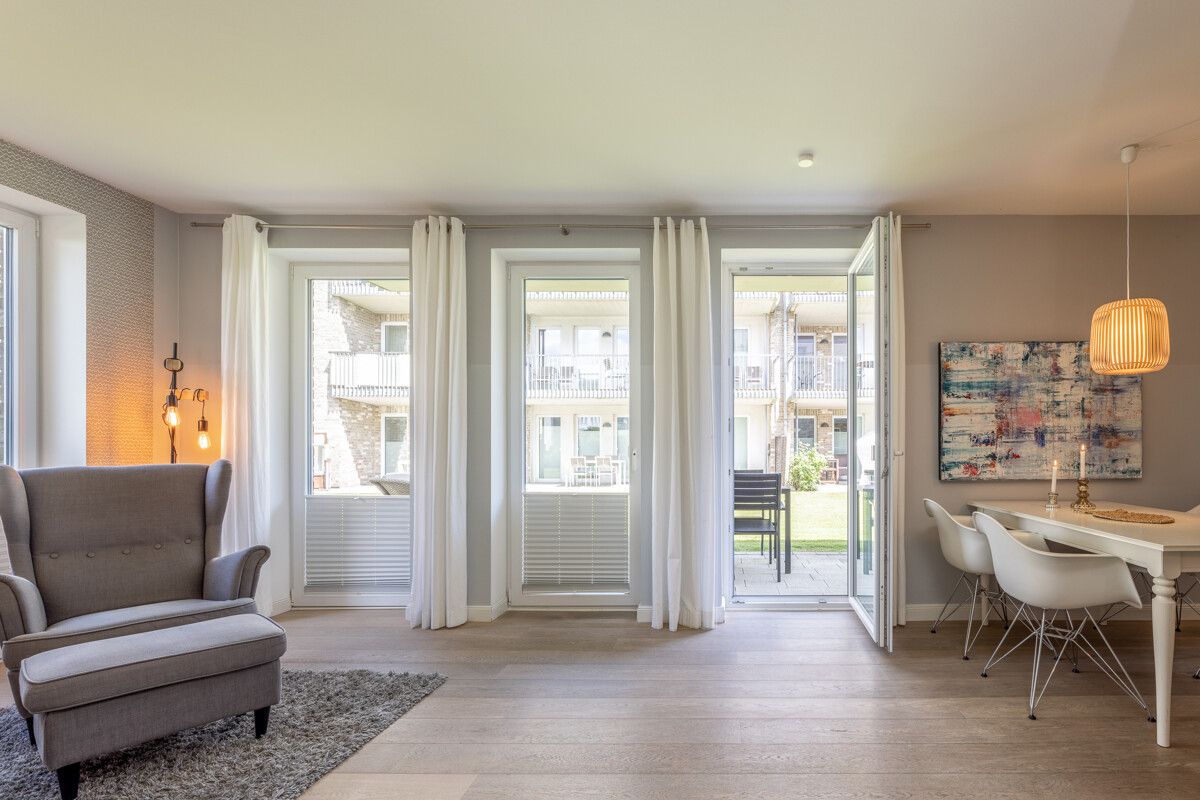 Helles Wohnzimmer mit Sessel, Esstisch, Stühlen und Zugang zur Terrasse durch große Fenster.