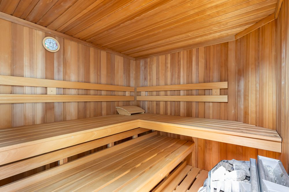Holzsauna mit Bänken, Ofen und einem Thermometer an der Wand.