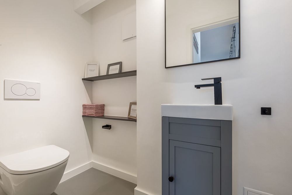 Modernes Badezimmer mit WC, Waschbecken, Spiegel und Wandregalen mit Dekoration.