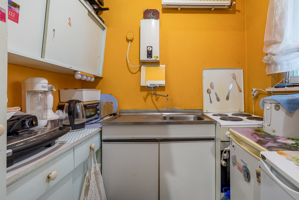 Kleine Küche mit gelben Wänden, Spüle, Herd, Toaster, Kaffeemaschine und Küchenschränken.