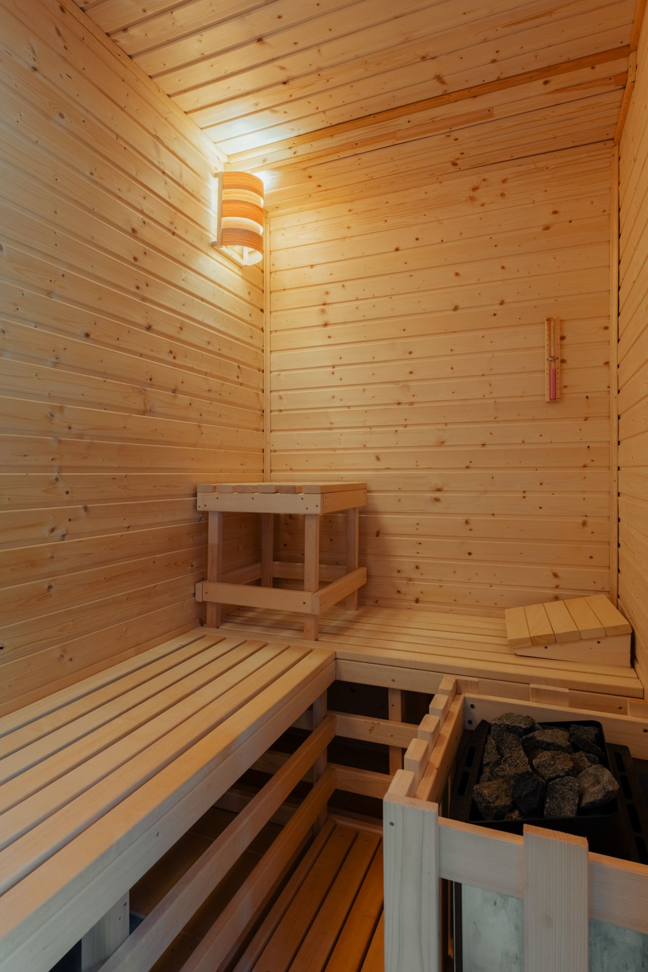 Helle Holzsauna mit Bänken, Lavasteinen und einer Wandleuchte.