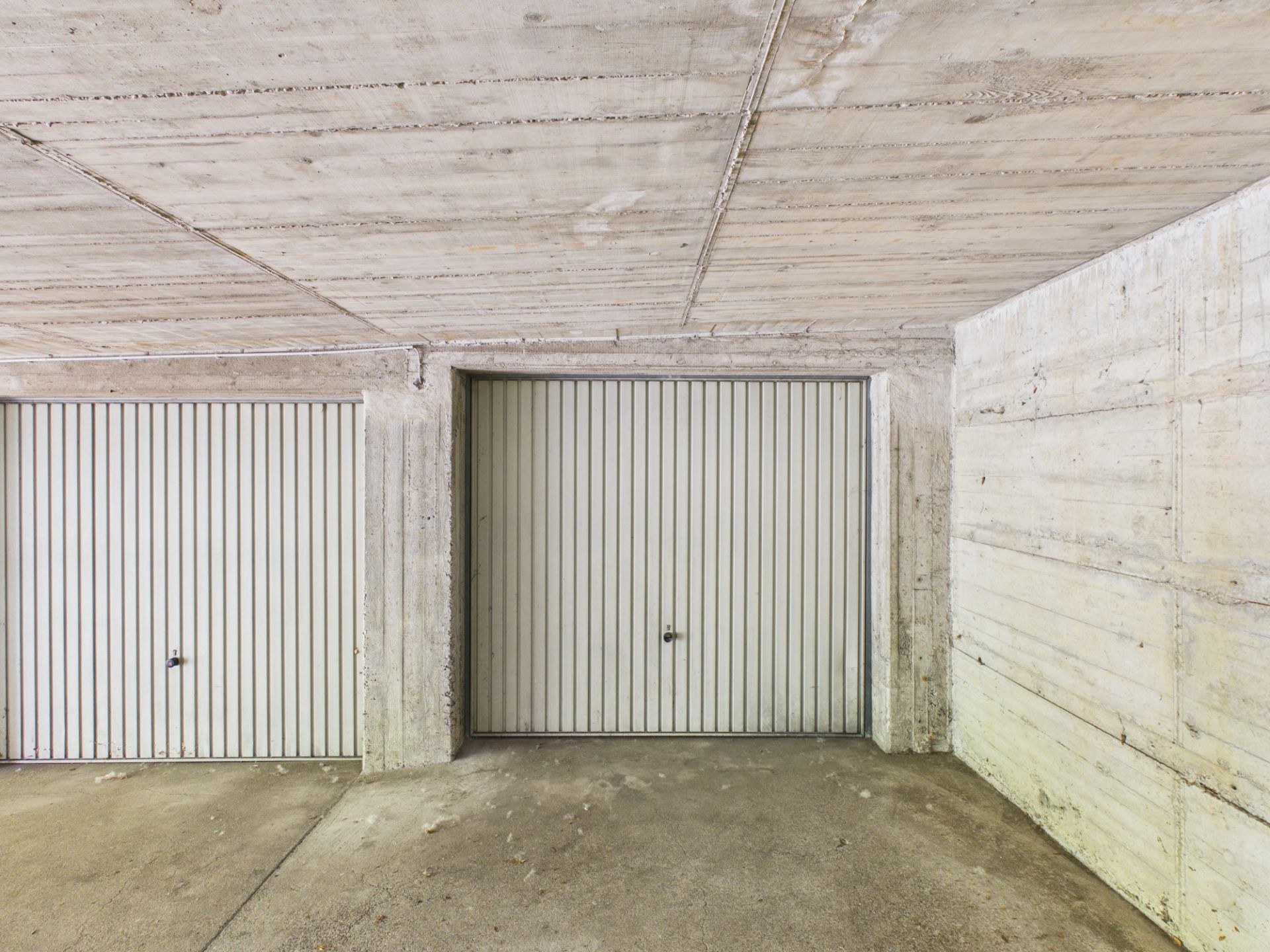 Drei geschlossene Garagentore aus Metall in einer Tiefgarage mit Betonwänden.