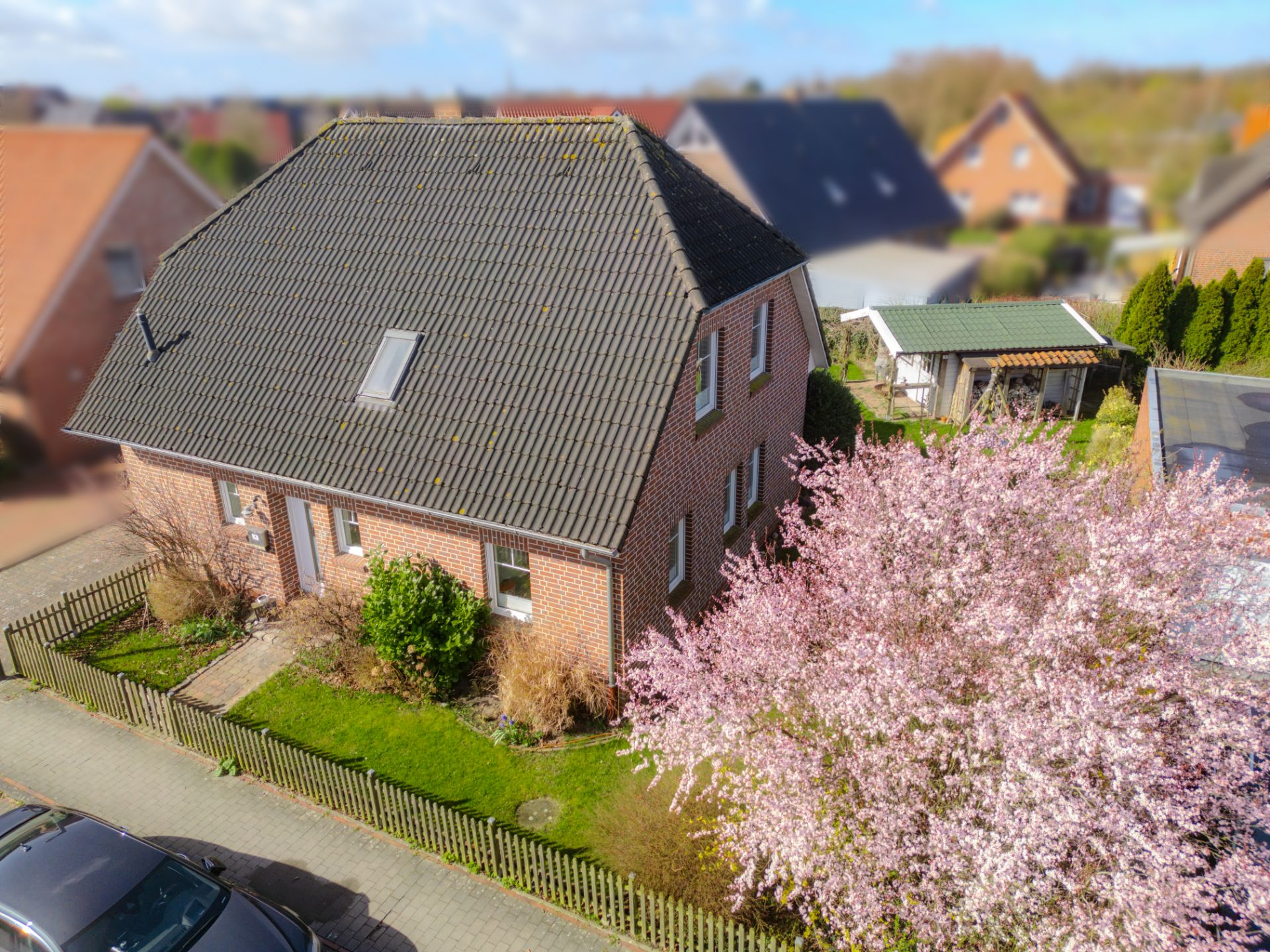 Backstein-Einfamilienhaus mit Garten, Blütenbaum und kleinem Zaun, Ansicht von oben.