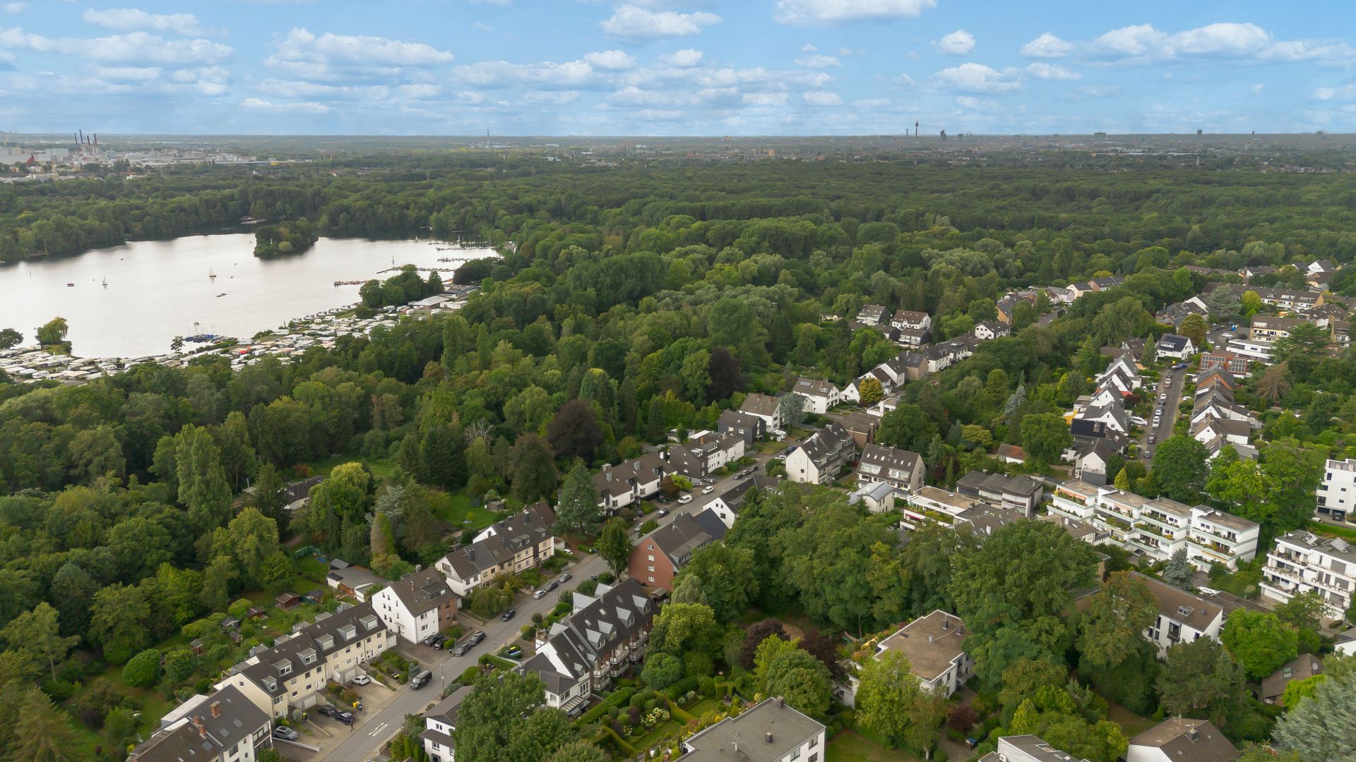 Luftaufnahme eines Wohngebiets mit vielen Häusern und Bäumen neben einem See.