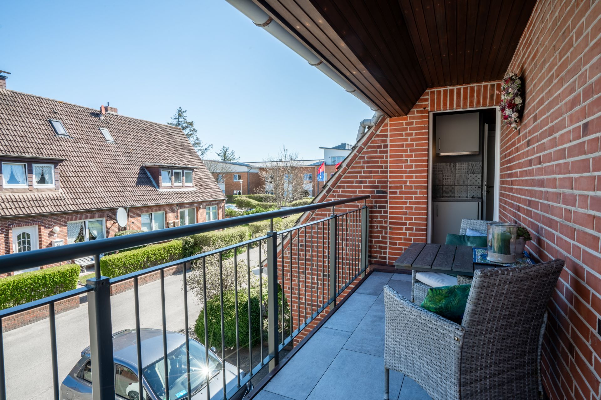 Balkon mit zwei Stühlen, einem Tisch und Blick auf Wohnhäuser und eine Straße.