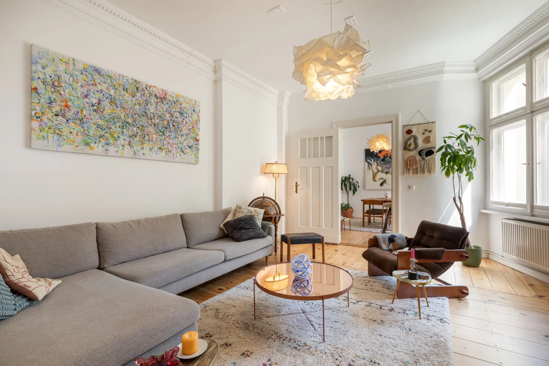 Helles Wohnzimmer mit grauem Sofa, Sessel, rundem Couchtisch und großem Fenster.