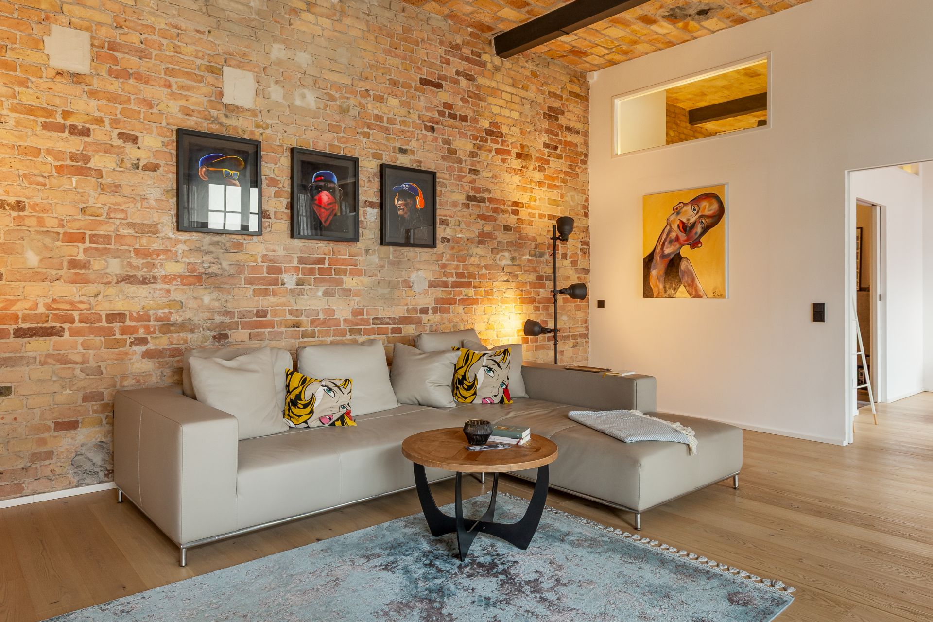Modernes Wohnzimmer mit Backsteinwand, grauem Sofa, bunten Kissen und Wandbildern.